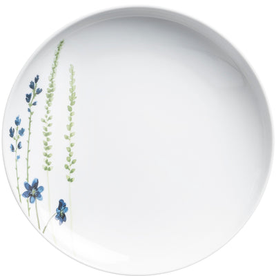 Ein runder Teller aus weißem Porzellan, verziert mit feinen, blauen Blumenmotiven und grünen Pflanzen im linken Bereich. Die florale Dekoration ist zart gestaltet, während der restliche Teller in schlichtem, unbeschichtetem Weiß gehalten ist. Ideal für elegante Tischdekorationen oder als Teil eines Geschirrsets.