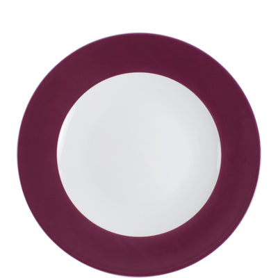Eine runde, flache Speiseteller mit einem mittleren, weißen Bereich und einem breiten Rand in tiefem Weinrot. Der Teller liegt flach auf einem weißen Hintergrund und zeigt eine klare und einfache Form, die für die Präsentation von Speisen geeignet ist.