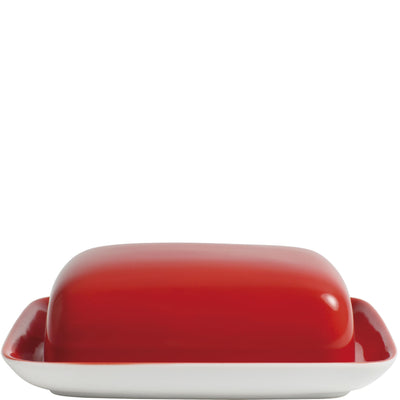 Ein roter Butterbehälter mit einem glatten, abgerundeten Deckel steht auf einem weißen, rechteckigen Untersetzer. Der Behälter hat eine glänzende Oberfläche und ist auf eine ansprechende Weise gestaltet, die sowohl funktional als auch dekorativ ist. Der Untersetzer hat eine leicht erhöhte Kante, die den Butterbehälter sicher hält. Die Kombination aus Rot und Weiß verleiht dem Set ein modernes und frisches Aussehen.