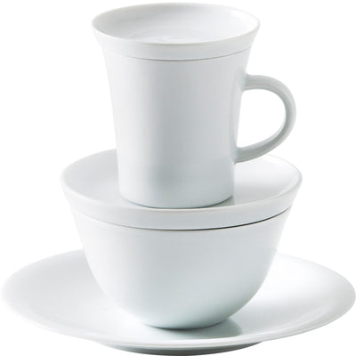 Eine weiße Tasse, die auf einer weißen Untertasse steht. Unter der Tasse befindet sich eine große, weiße Schüssel mit einem geschlossenen Deckel. Alle Teile haben ein schlichtes, modernes Design und sind aus glänzendem Keramikmaterial gefertigt. Der Hintergrund ist neutral gehalten, sodass die Geschirrteile im Fokus stehen.