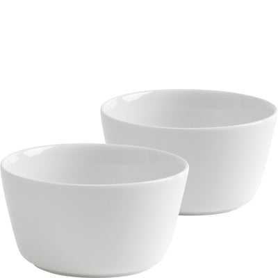Zwei schlichte, weiße Schalen aus Keramik, eine größere Schale im Vordergrund und eine kleinere im Hintergrund. Beide Schalen haben eine runde Form und sind glatt. Sie stehen auf einer hellen Oberfläche, die den minimalistischen Look unterstreicht.