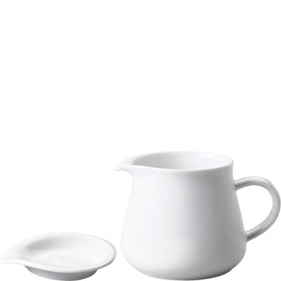 Ein weißes Porzellan-Kännchen mit einem kleinen Unterteller. Das Kännchen hat eine runde Form, einen geschwungenen Ausguss und einen praktischen Henkel. Der Unterteller hat eine flache, runde Form und dient als Ablage für das Kännchen. Die Oberfläche des Geschirrs ist glatt und glänzend, was ihm ein modernes und elegantes Aussehen verleiht.