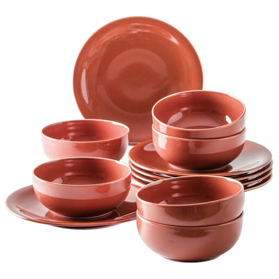 Eine Sammlung von Geschirr in einem einheitlichen, terrakottafarbenen Design. Im Vordergrund sind mehrere Schalen unterschiedlicher Größen zu sehen, zusammen mit zwei kleineren Schalen. Im Hintergrund stehen mehrere flache Teller, die übereinander gestapelt sind. Das Geschirr hat eine glänzende Oberfläche und ist auf einem hellen Untergrund angeordnet.