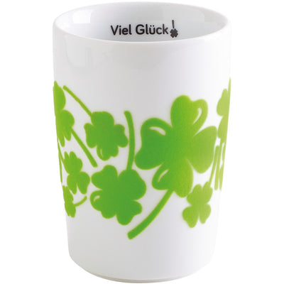 Weißer Becher mit grünen Klee-Motiven und der Aufschrift "Viel Glück" im oberen Rand. Der Becher hat eine schlichte, elegante Form und ist ideal für Getränke oder als Geschenk.