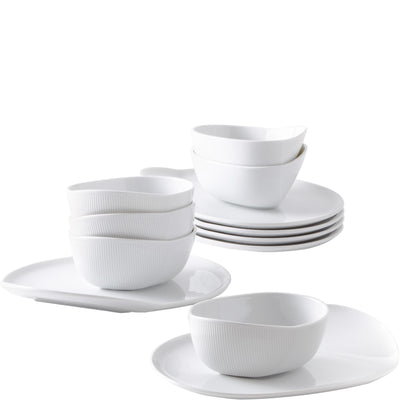 Eine Auswahl an weißen Geschirrteilen auf einem weißen Hintergrund. Im Vordergrund liegt ein flacher Teller, darauf sind zwei tiefere Schalen mit einer gerippten Oberfläche angeordnet. Im Hintergrund stapeln sich mehrere flache Teller. Die gesamte Geschirrserie ist elegant und minimalistisch gestaltet, geeignet für festliche Anlässe oder den täglichen Gebrauch.