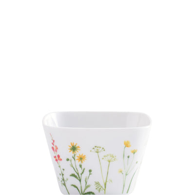 Weiße, viereckige Schale mit buntem Blumenmuster. Die Außenseite zeigt verschiedene wild wachsende Pflanzen in Farben wie Rot, Gelb und Grün. Die Schale hat eine glatte Oberfläche und einen schlichten, modernen Look, der sie ideal für eine stilvolle Präsentation von Snacks oder Dips macht.