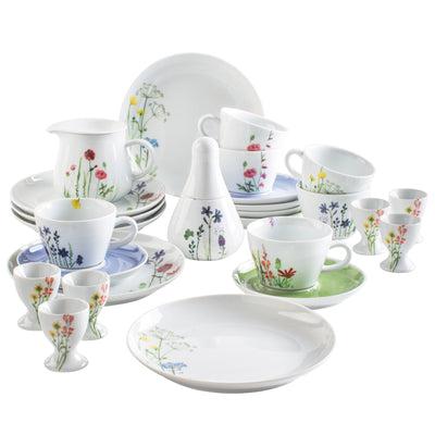 Ein Set aus weißem Geschirr mit bunten Blumenmotiven. Zu sehen sind verschiedene Tassen, Teller, eine Kaffeekanne, Zuckergefäß und Eierbecher. Die Tassen sind in verschiedenen Größen angeordnet, während die großflächigen Teller im Vordergrund liegen. Die floralen Muster verleihen dem Geschirr eine fröhliche und lebendige Optik, ideal für festliche Anlässe oder den täglichen Gebrauch.