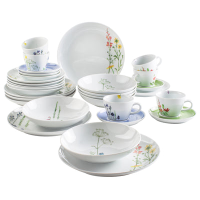 Eine Sammlung von Geschirr, bestehend aus weißen Tellern, Schalen und Tassen mit bunten, floralen Motiven. Im Vordergrund sind mehrere flache Teller, Schalen und unterschiedliche Tassen mit passenden Untertassen angeordnet. Im Hintergrund sind weitere Geschirrteile gestapelt. Die floralen Designs verleihen dem Geschirr eine fröhliche und lebendige Ausstrahlung.