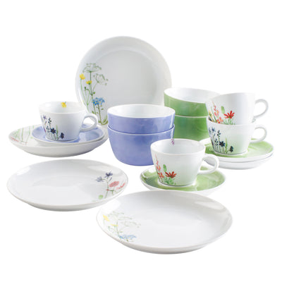 Eine helle, floral dekorierte Geschirrkollektion, bestehend aus mehreren Tellern, Untertassen und Tassen in verschiedenen Farben, darunter Blau und Grün. Die Motive zeigen zarte Blumenmuster auf weißem Porzellan. Die Tassen sind teilweise gestapelt, während die größeren Teller flach liegen. Diese Anordnung vermittelt einen fröhlichen, einladenden Eindruck.