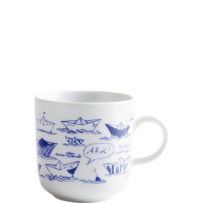 Eine weiße Keramiktasse mit blauen Illustrationen von Papierbooten und Wasserwellen. Auf der Tasse steht das Wort "Ahoi" in einer Sprechblase, sowie der Name "Maria" in verspielter Schrift. Die Tasse hat einen einfachen Henkel und ist auf einer hellen Oberfläche platziert. Sie vermittelt ein maritimes und fröhliches Gefühl.