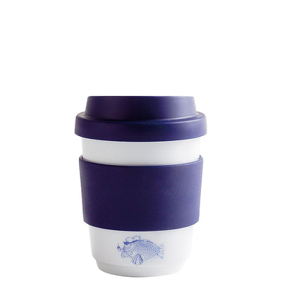 Ein wiederverwendbarer Kaffeebecher aus Keramik mit einem weißen unteren Teil und einem dunkelblauen Silikonring. Der Becher hat einen Deckel in derselben Farbe und zeigt eine blaue Illustration eines Fisches auf der Vorderseite. Der Becher steht auf einer weißen Oberfläche und vermittelt einen umweltfreundlichen Eindruck.