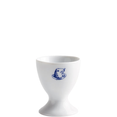 Ein keramisches Ei-Halterchen in Weiß, mit einem blauen, humorvollen Frosch-Design auf der Frontseite. Der Halter hat eine schmale Basis und eine breitere, nach oben offene Form, die für den sicheren Halt eines gekochten Eis dient. Der Frosch ist freundlich und trägt ein kleines Stück Essen.