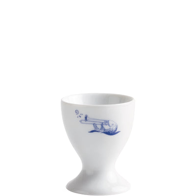 Ein weißes Eierbecher aus Porzellan mit einem blauen, handgezeichneten Motiv eines Fisches, der ein Horn bläst. Der Becher hat eine klassische Form mit einem weit geöffneten oberen Rand und einem schmalen, stabilen Fuß. Das Design kombiniert humorvolle Illustrationen mit funktionalem Design, geeignet für den Alltag.