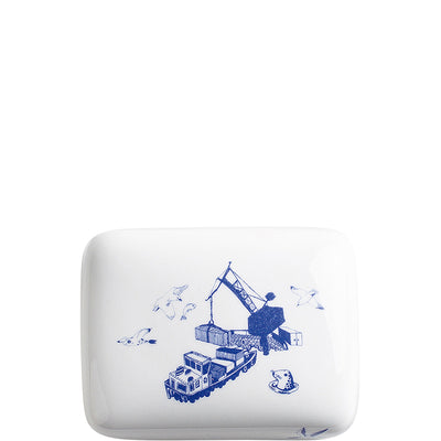 Eine weiße Keramik-Butterdose mit blauem Dekor, das ein Frachtschiff im Hafen zeigt. Um das Schiff herum fliegen Vögel, und ein Kran hebt Kisten.
