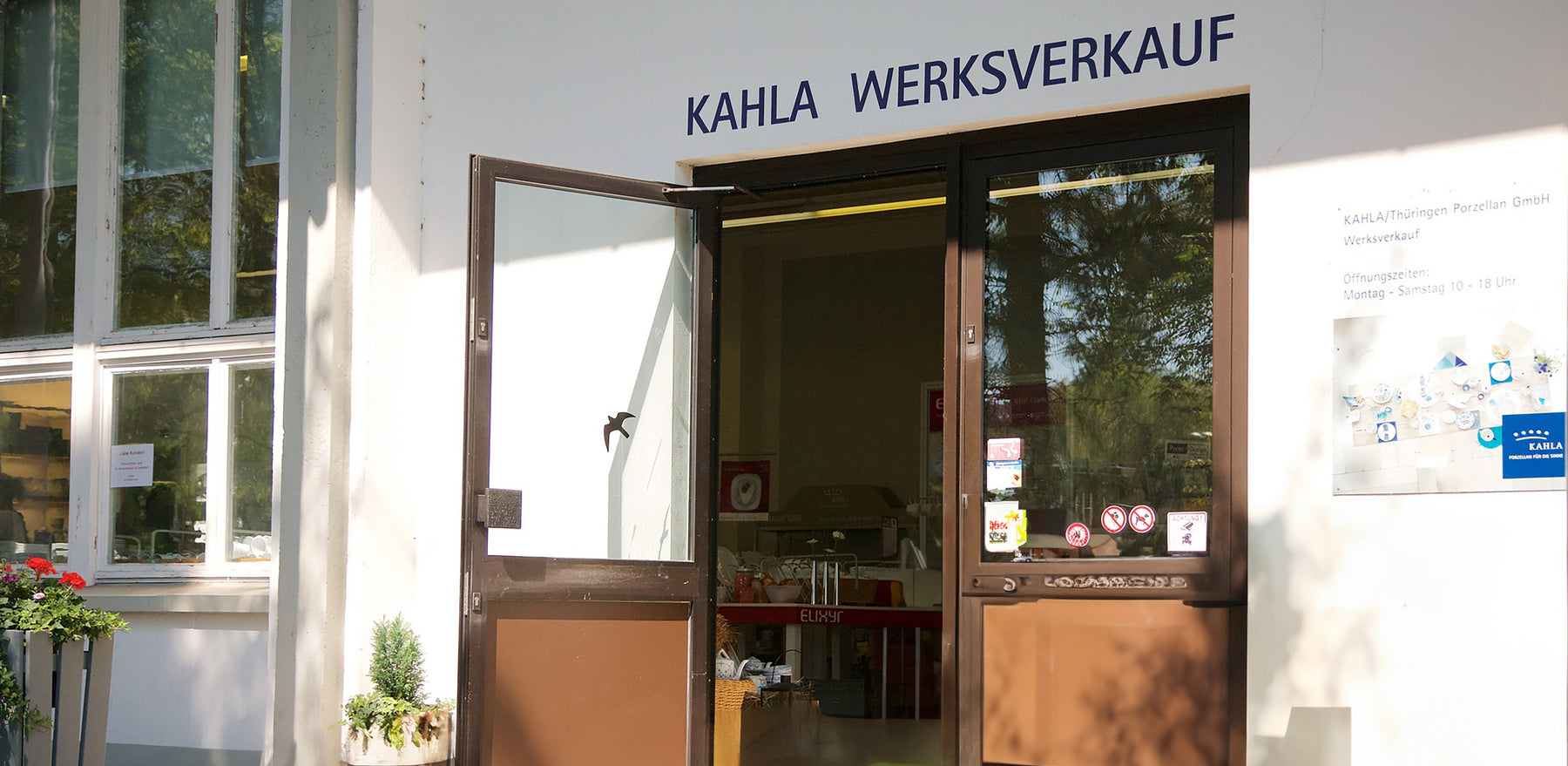 Ein Blick auf den Eingang des Kahla Werksverkaufs. Die doppelflügelige Tür ist geöffnet und lädt zum Betreten ein. Rechts ist ein Schild mit dem Schriftzug 
